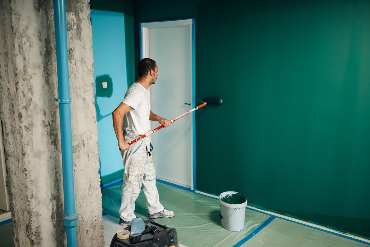 Professional painter using a paint roller applying green paint on a wall