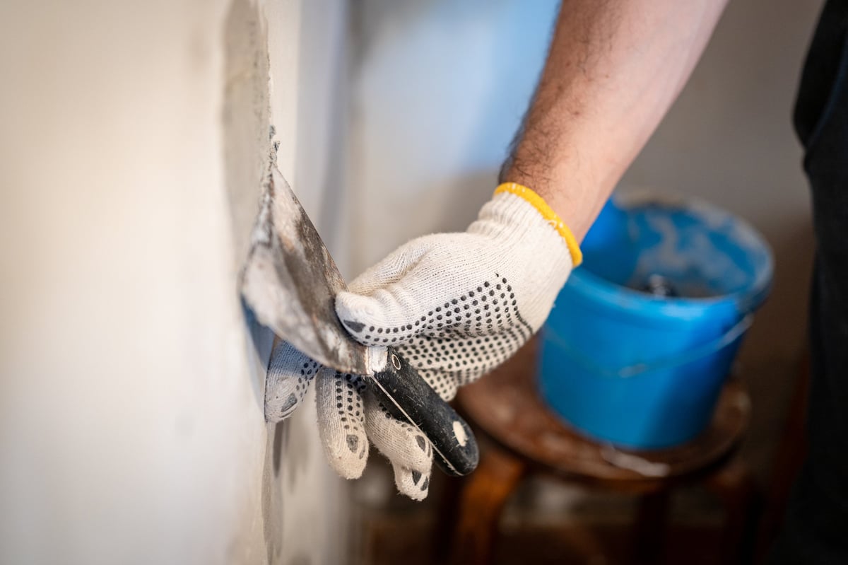 Worker using putty knife to press patching compound into a hole in interior wall